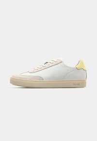 White leather sneakers with gray suede accents, cream laces, yellow heel tab, and textured rubber sole. Side profile view.