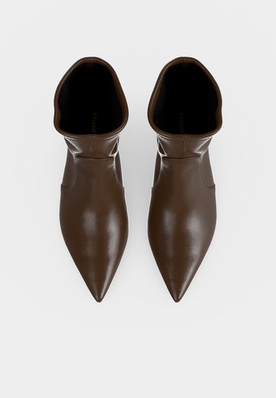 Paire de bottines marron à bout pointu en cuir lisse, vues de dessus sur fond blanc.
