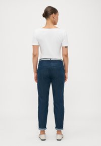 Un haut blanc à manches courtes associé à un jean tapered bleu foncé, avec des revers et un design de ceinture contrastant.