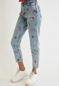Jasnoniebieskie jeansy denimowe z kwiatową haftem w kolorach czerwonym, żółtym i zielonym. Posiadają wysoki stan i zwężane nogawki o długości do kostek. Stylizowane z białymi trampkami.