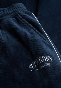 Nachtblaues Cord-Jogginghosen mit weißen seitlichen Streifen und gesticktem "SUPERDRY"-Logo. Strukturiertes Material mit elastischem Bund und seitlichen Taschen.