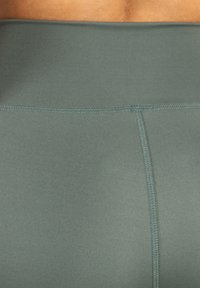 Tmavě zelené legíny na aktivní nošení mají hladkou, elastickou tkaninu s vypasovaným střihem a jemnými detaily v švech.