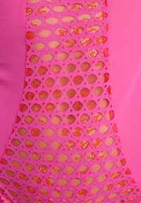 Roze zwempak met een groot gaaspaneel met ovale uitsparingen, waardoor een gestructureerde laag eronder zichtbaar is. Soepele stof met een glanzende afwerking.