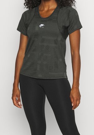 Kobieta ubrana w czarną sportową koszulkę Nike Air z krótkim rękawem i wzorem oraz czarne legginsy, stojąca na jednolitym tle.
