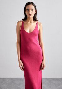 Abito a maglia fucsia aderente con spalline sottili, scollatura profonda e spacco laterale. Realizzato in tessuto morbido e testurizzato con una finitura liscia.
