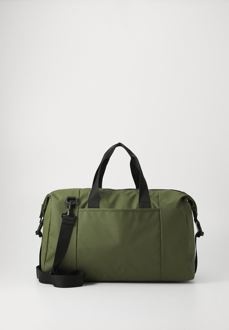 Sac de sport vert en tissu durable. Équipé de poignées noires, d'une sangle ajustable et d'une poche avant. Forme structurée avec une texture lisse.