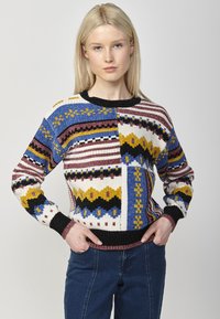 Pull en tricot avec un motif géométrique multicolore en bleu, jaune, rouge et noir, avec un col et des poignets côtelés.