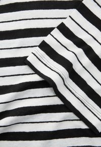 Black and white striped fabric with alternating bold stripes. Soft texture with visible stitching along the edges and sleeve.