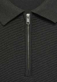Polo negru tricotat, cu un design texturat și deschis, având un fermoar argintiu la gât. Prezintă un guler clasic.