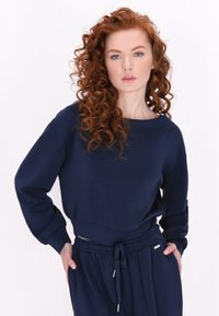 Felpa blu navy con vestibilità ampia, scollo rotondo e maniche lunghe. Il tessuto appare morbido; presenta una vita elasticizzata e un cordoncino.