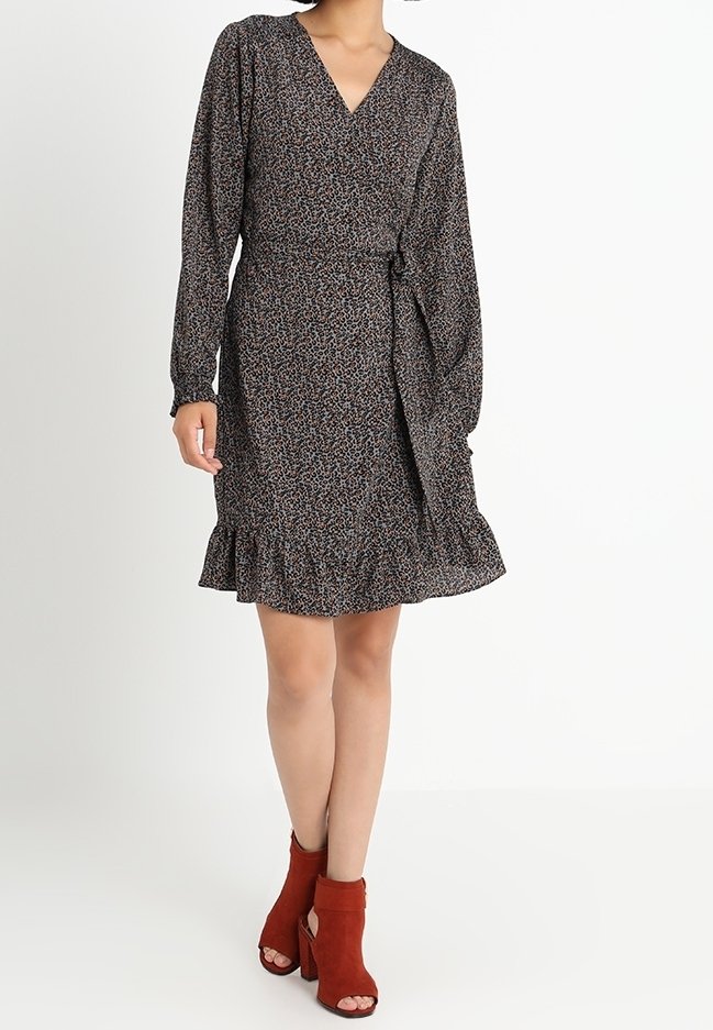 Robe noire à manches longues, avec un ourlet volanté et un motif floral. Associée à des bottes à talons avec une bride de cheville rouge. Texture de tissu lisse.
