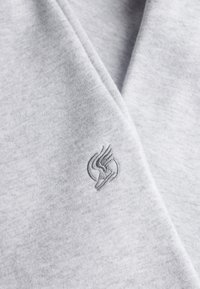 Tissu gris clair doux avec un logo délicat de chaussure ailée brodé près d'une couture.