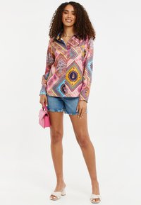 Farverig langærmet skjorte med et geometrisk mønster, knap-front design, sammensat med denimshorts og en lille lyserød håndtaske.
