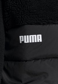 Zwarte jas met een donzige textuur aan de bovenkant en een gladde onderkant, voorzien van een opvallend wit "PUMA" logo in blokletters.