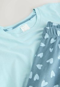 Valkoinen puuvillainen t-paita, jossa on pyöreä kaulus, yhdistettynä harmaisiin shortsit, joissa on valkoinen sydänkuvio. Pehmeä pinta, rento muotoilu.