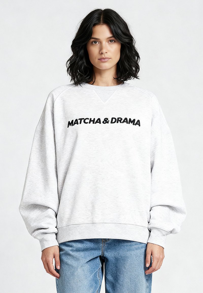 Felpa grigio chiaro con polsini e orlo a coste, con la scritta nera audace "MATCHA & DRAMA" sul davanti. Design a vestibilità ampia.