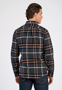 Mörkrutig skjorta i grå, vit och rostfärgade nyanser. Tillverkad av texturerat tyg med långa ärmar och knappmanschetter. Visad bakifrån.