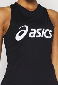 Osoba ubrana w czarny sportowy top bez rękawów z dużym, białym logo Asics umieszczonym na środku klatki piersiowej.