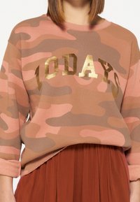 Felpa mimetica marrone e rosa con lettering dorato "TODAYS", caratterizzata da una vestibilità comoda e una texture morbida. Maniche lunghe con orli arrotolati.