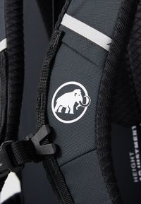 Svart stoff ryggsekkstropp med sølv detaljer, med et hvitt elefantlogo og en plastspenne for justering.