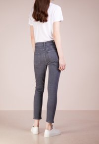 Jeans de mezclilla gris, de tiro alto, ajustados, con dos bolsillos traseros y un ligero stretch. Combinados con una camiseta blanca y zapatillas blancas.