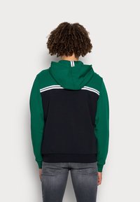 Sweatshirt con cappuccio caratterizzato da sezioni verdi e nere, strisce bianche lungo la schiena e un tessuto testurizzato. Design aderente con polsini a coste.