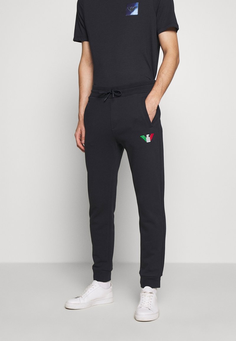 Black joggers made of cotton blend fabric, featuring an elastic waistband, side pockets, and a multicolor embroidered logo on the left hip.