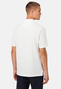 Bílé polo tričko s krátkým rukávem, texturovaná tkanina, plochý límec a nášivka s logem na zadní části krku. Má boční štěrbiny na lemu.