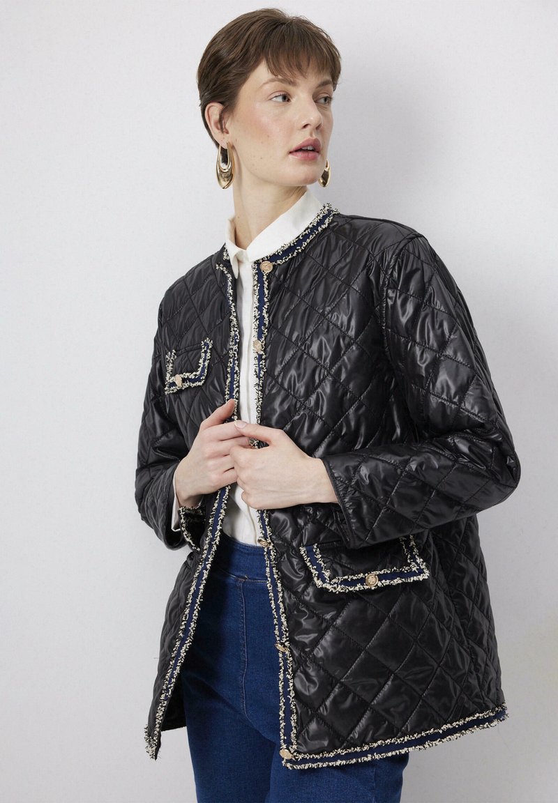 Black quilted jacket with a textured finish, trimmed in light contrast thread, featuring two patch pockets and gold-tone buttons.