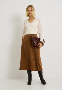 Haut à manches longues en dentelle crème avec un col festonné, jupe midi en suède marron et sac à main en cuir bordeaux clouté ; bottes noires jusqu'aux genoux.