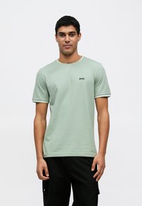 Camiseta de algodão verde com mangas curtas, decote redondo e logótipo a preto. Apresenta um acabamento contrastante no decote e nas mangas.