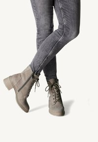 Des bottines grises à lacets à l'avant, avec des zips sur les côtés, un dessus texturé et un talon épais, assorties à un jean skinny gris.
