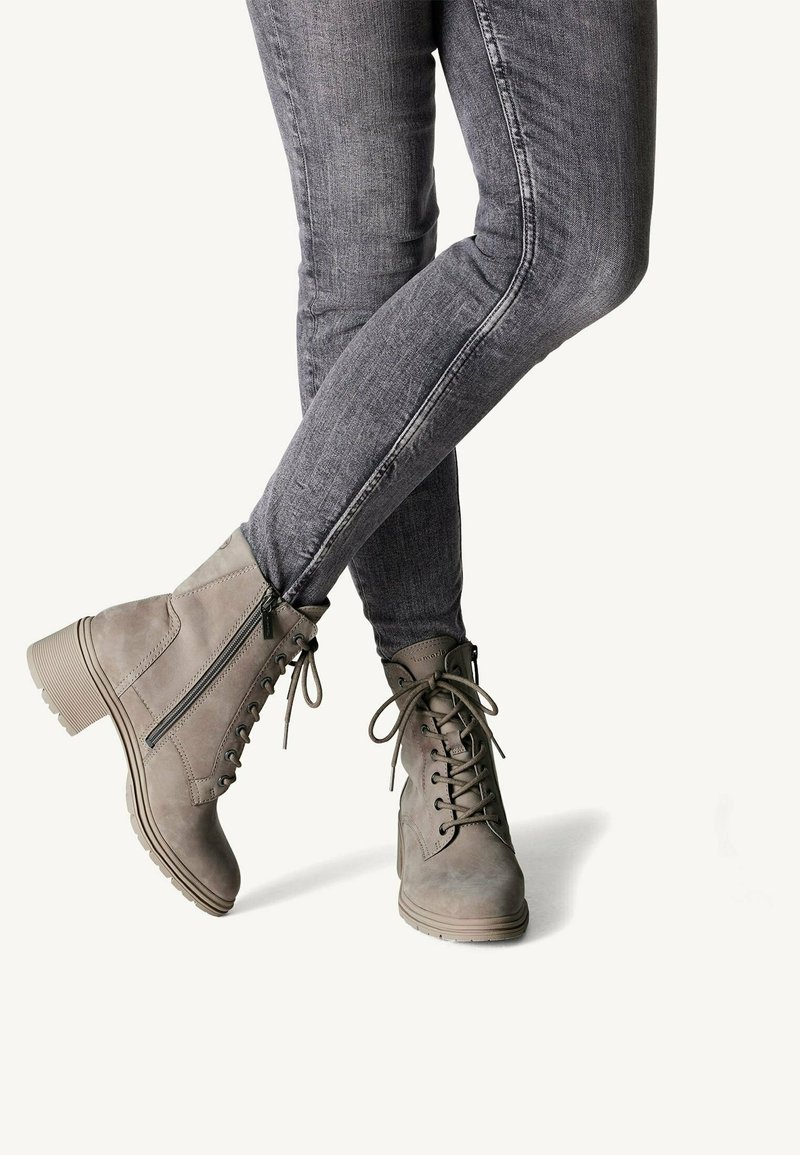 Des bottines grises à lacets à l'avant, avec des zips sur les côtés, un dessus texturé et un talon épais, assorties à un jean skinny gris.