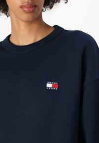 Felpa in cotone blu navy con colletto a costine, dotata di un piccolo logo ricamato "TOMMY JEANS" in rosso, bianco e blu sul petto.