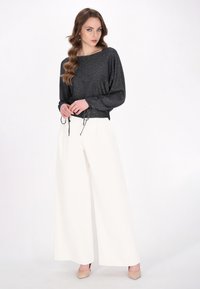 Zwart, sprankelende pullover met een losse pasvorm, drawstring taille; gecombineerd met witte broek met wijde pijpen; model draagt blote hoge hakken.