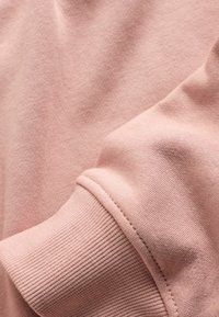 Hellrosa Sweatshirt-Stoff mit weicher Textur. Verfügt über ein geripptes Bündchendetail und glatte Nähte entlang der Kanten.
