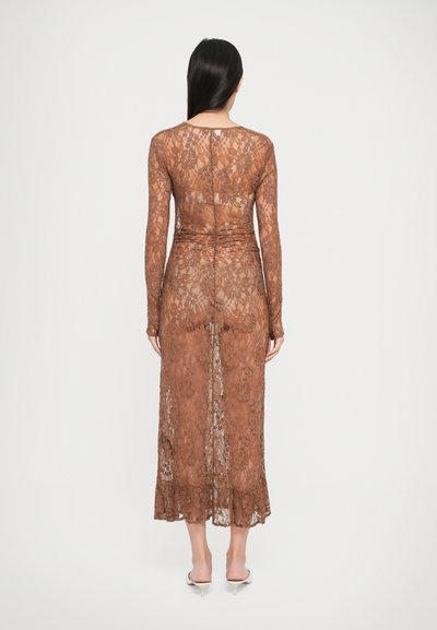 Robe longue en dentelle brune transparente avec des manches longues, une taille froncée et un ourlet à volants. Présente des motifs floraux et une fente dans le dos.