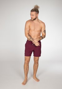 Bordeaux zwembroek met horizontale strepen, trekkoord in de taille en zijzakken, getoond op een naakt bovenlijf mannelijk model.