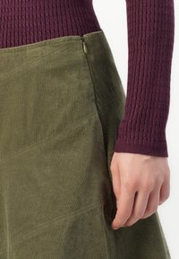Grön kordskjol med diagonala sömdetaljer och dragkedja på sidan, kombinerad med en vinröd ribbad topp med lång ärm.