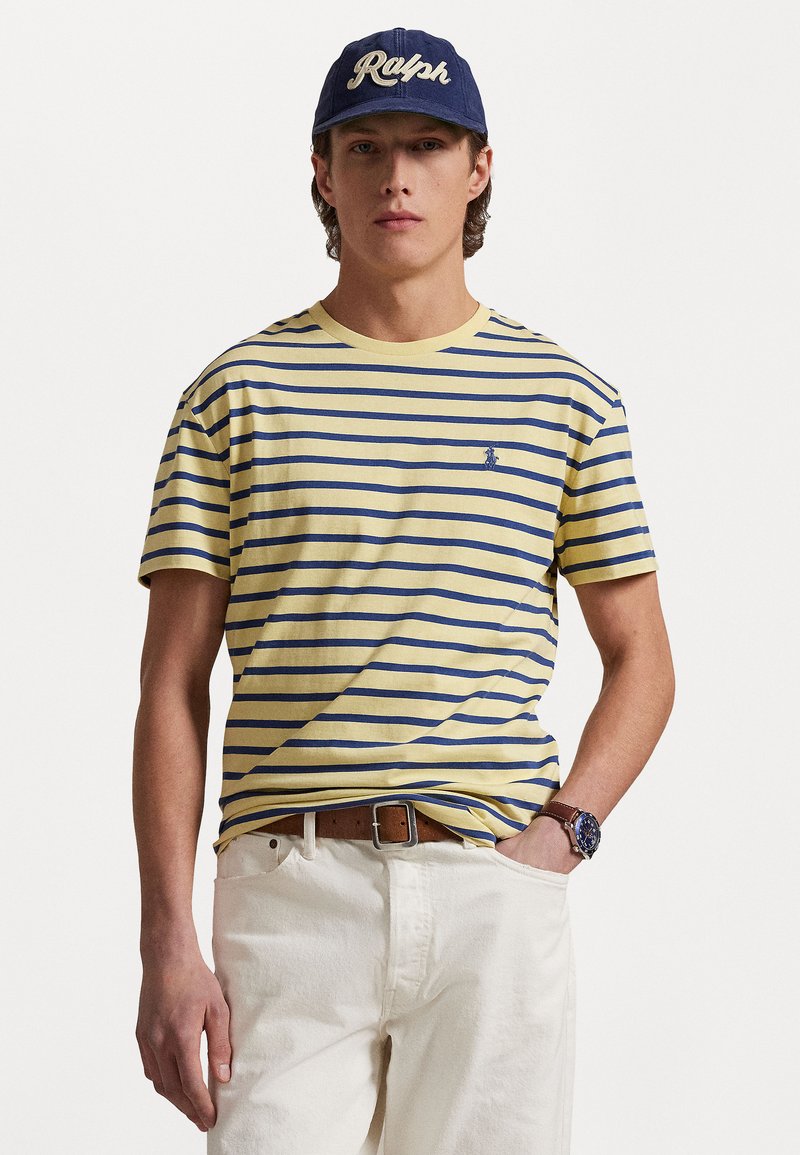 Κίτρινη και ναυτική ριγέ μπλούζα με κοντά μανίκι�α και λαιμόκοψη τύπου crew; διαθέτει ένα μικρό λογότυπο στο στήθος. Φοριέται με ανοιχτόχρωμα τζιν.