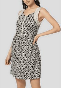 Vestido de estampado en blanco y negro con formas de diamante, que presenta un frente abotonado y tirantes beige. Tejido suave con un ajuste relajado.