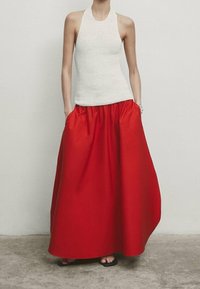 Haut halter en tricot blanc associé à une jupe rouge fluide taille haute, avec des poches latérales et une texture lisse.