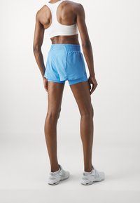 Pantalones cortos deportivos azul con cintura elástica, textura suave y corte ajustado, combinados con un sujetador deportivo blanco y zapatillas gris claro.