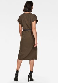 Vestido verde oliva con mangas cortas y un corte relajado, que cuenta con un cinturón negro en la cintura, extendiéndose por debajo de la rodilla.