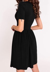 Vestido negro con mangas cortas, corsé ajustado y falda con fruncidos. Hecho de una tela suave con textura lisa. Cuello redondo simple.
