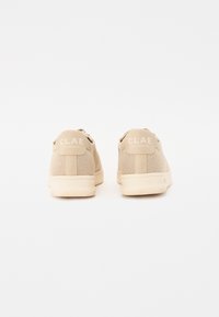 Sneaker beige con tomaia in rete testurizzata, collo imbottito e suola in gomma. Presenta un logo sul tallone e una chiusura con lacci.