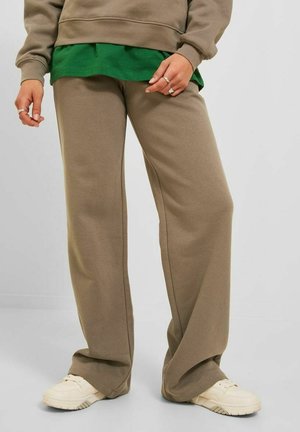 Tan joggebukser i mykt materiale med vid ben design. Kombinert med en grønn lagdelt skjorte, komplementert av hvite joggesko.
