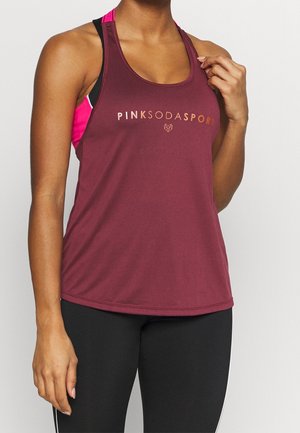 Kobieta nosząca bordowy sportowy top bez rękawów z logo "Pink Soda Sport" oraz czarne legginsy, poprawia pasek topu prawą ręką.