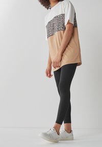 Kortærmet t-shirt med hvid top, leopardmønster i midten og tan bund. Sat sammen med sorte leggings og hvide sneakers.