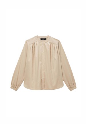 Blouse beige à manches longues en tissu doux et lisse, avec un col rond, un devant à boutons et des détails froncés aux épaules.